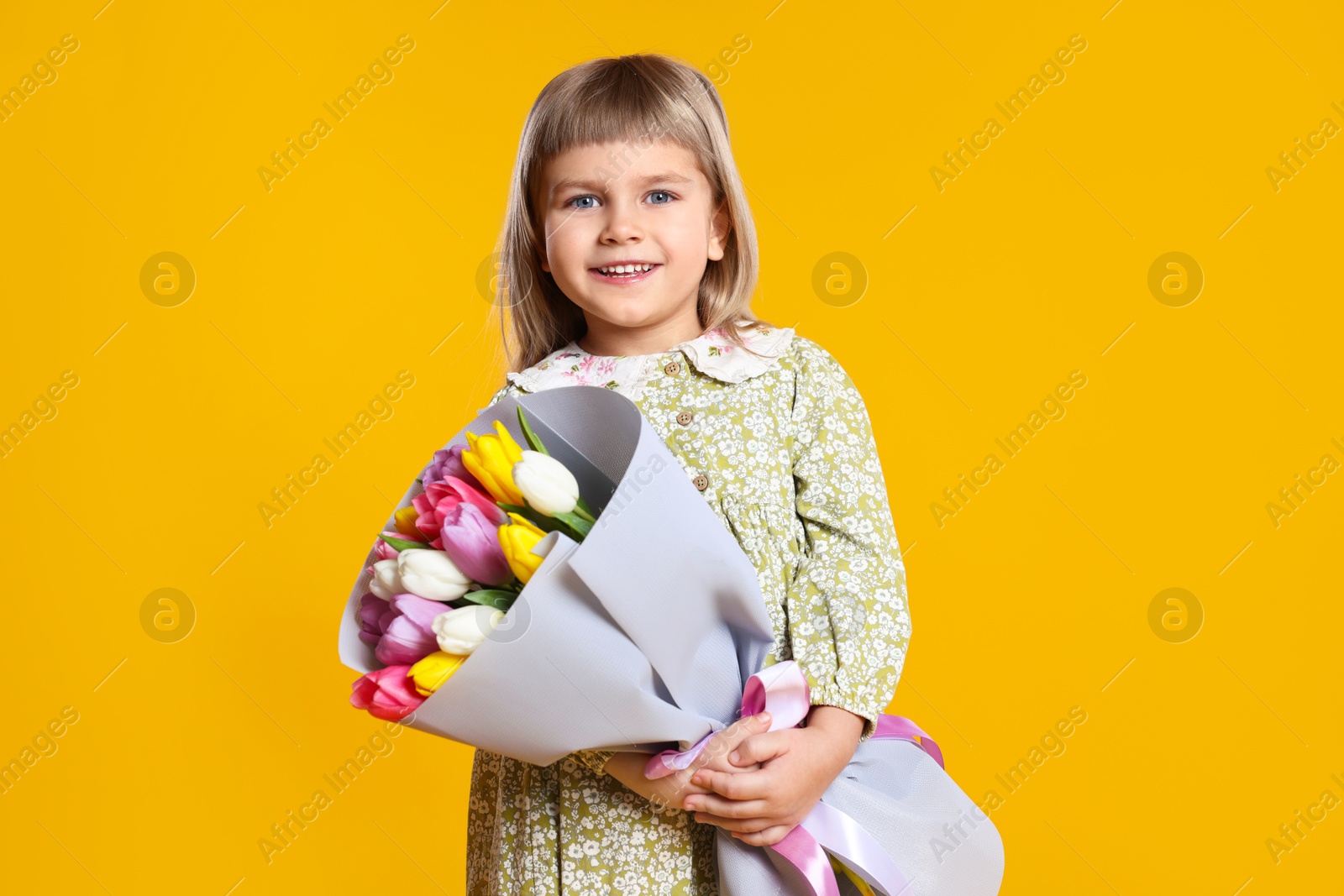 Photo of Smiling little girl with bouquet of tulips on orange background