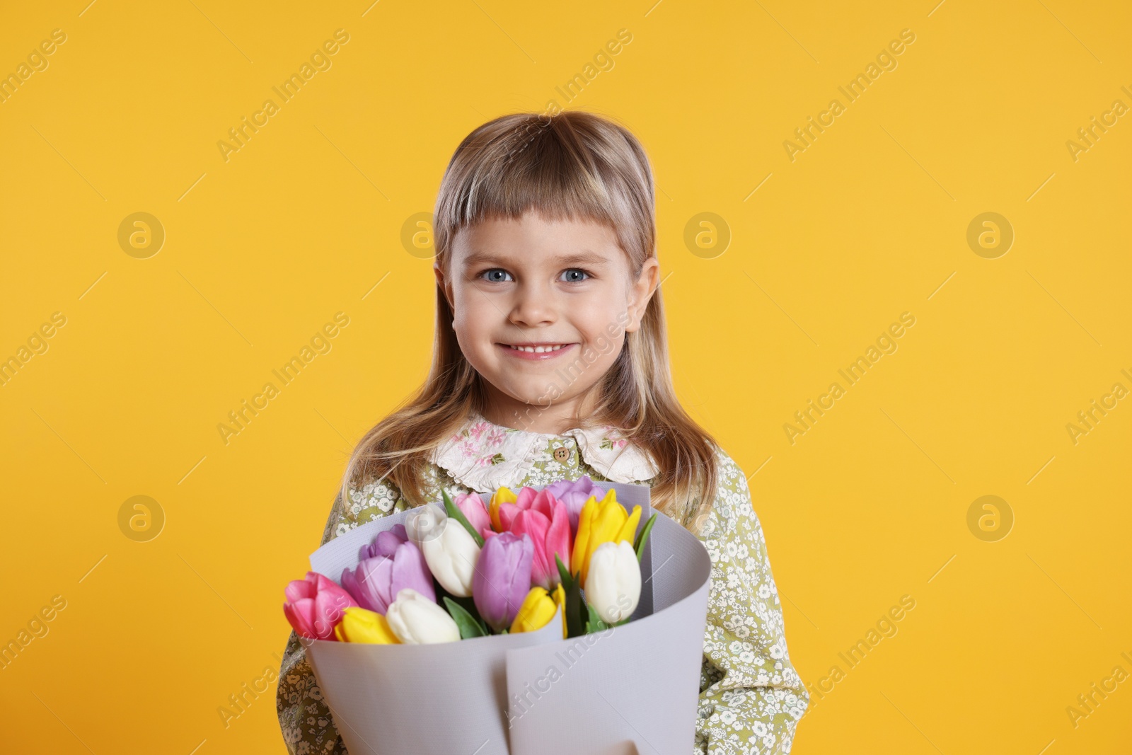 Photo of Smiling little girl with bouquet of tulips on orange background