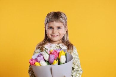 Photo of Smiling little girl with bouquet of tulips on orange background