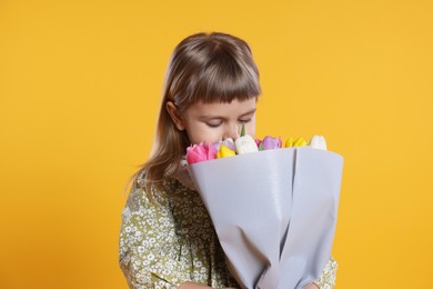 Photo of Cute little girl smelling bouquet of tulips on orange background