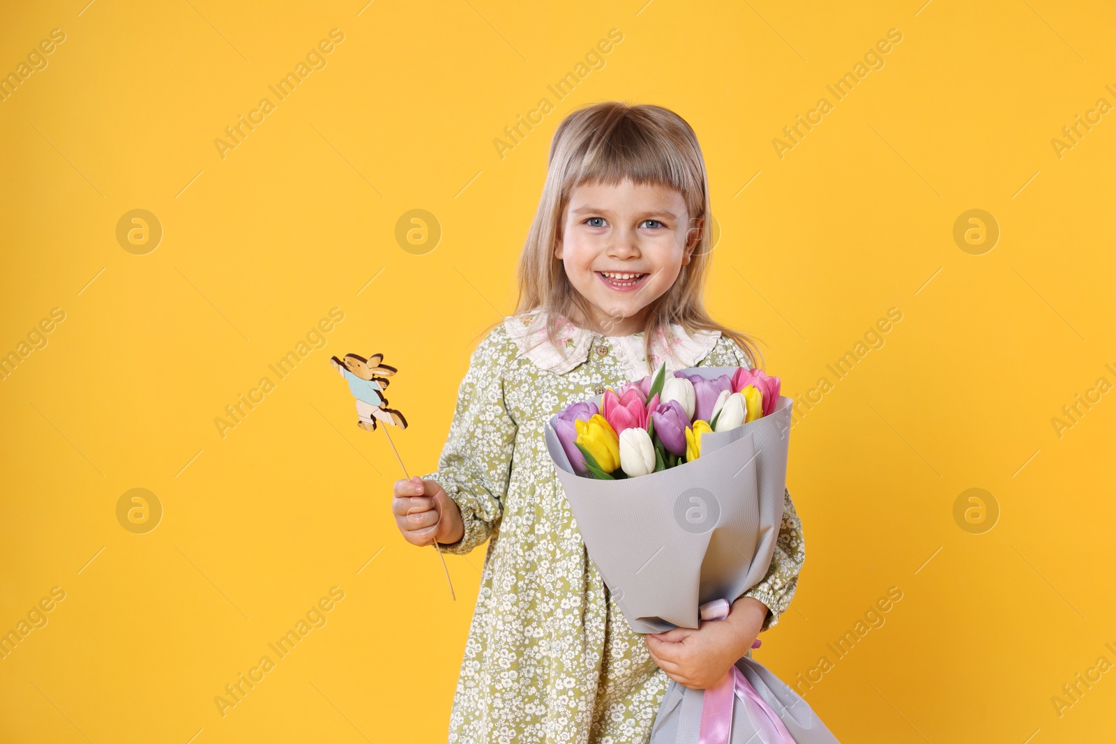 Photo of Smiling little girl with bouquet of tulips and decorative Easter bunny on orange background