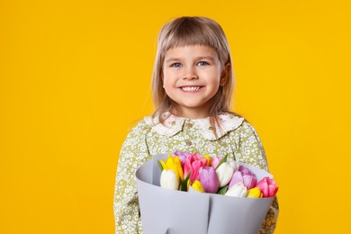 Photo of Smiling little girl with bouquet of tulips on orange background. Space for text