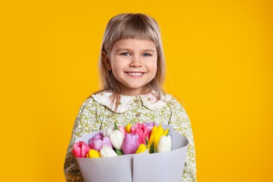 Photo of Smiling little girl with bouquet of tulips on orange background