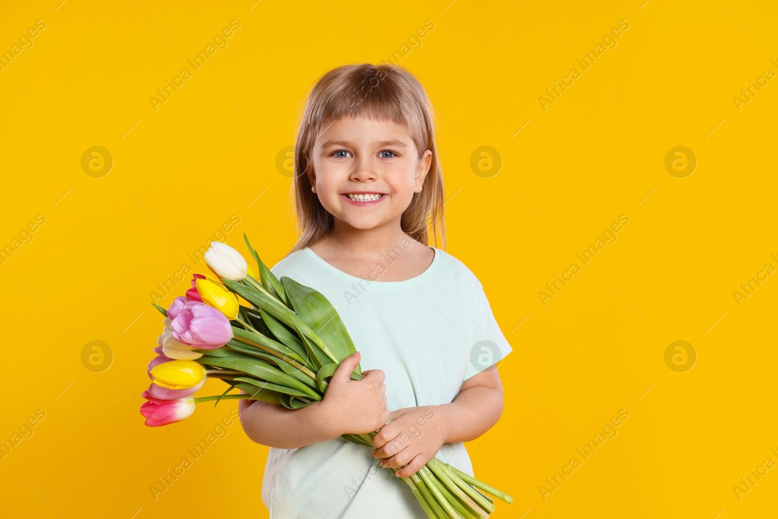 Photo of Smiling little girl with bouquet of tulips on yellow background