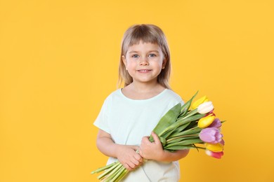 Photo of Smiling little girl with bouquet of tulips on yellow background. Space for text