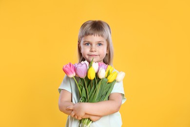 Photo of Cute little girl with bouquet of tulips on yellow background