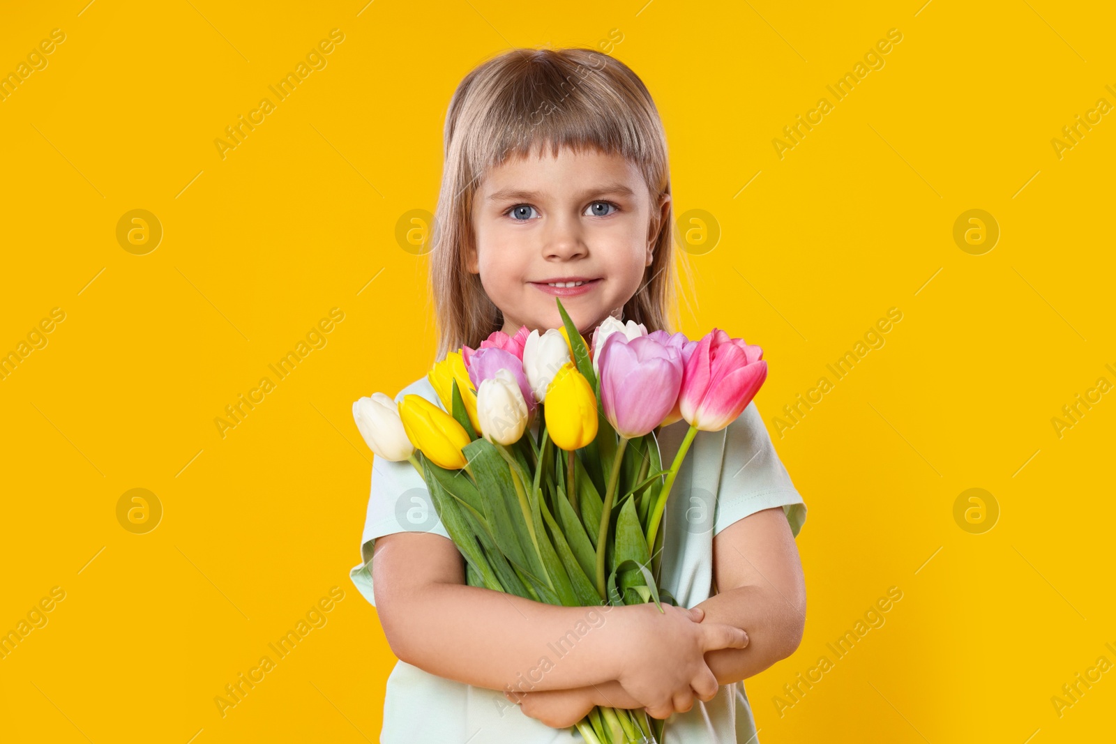 Photo of Smiling little girl with bouquet of tulips on yellow background. Space for text