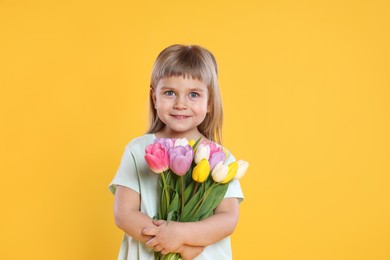 Photo of Smiling little girl with bouquet of tulips on yellow background