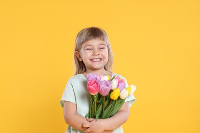 Photo of Smiling little girl with bouquet of tulips on yellow background