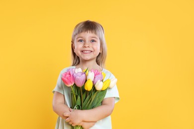 Photo of Smiling little girl with bouquet of tulips on yellow background