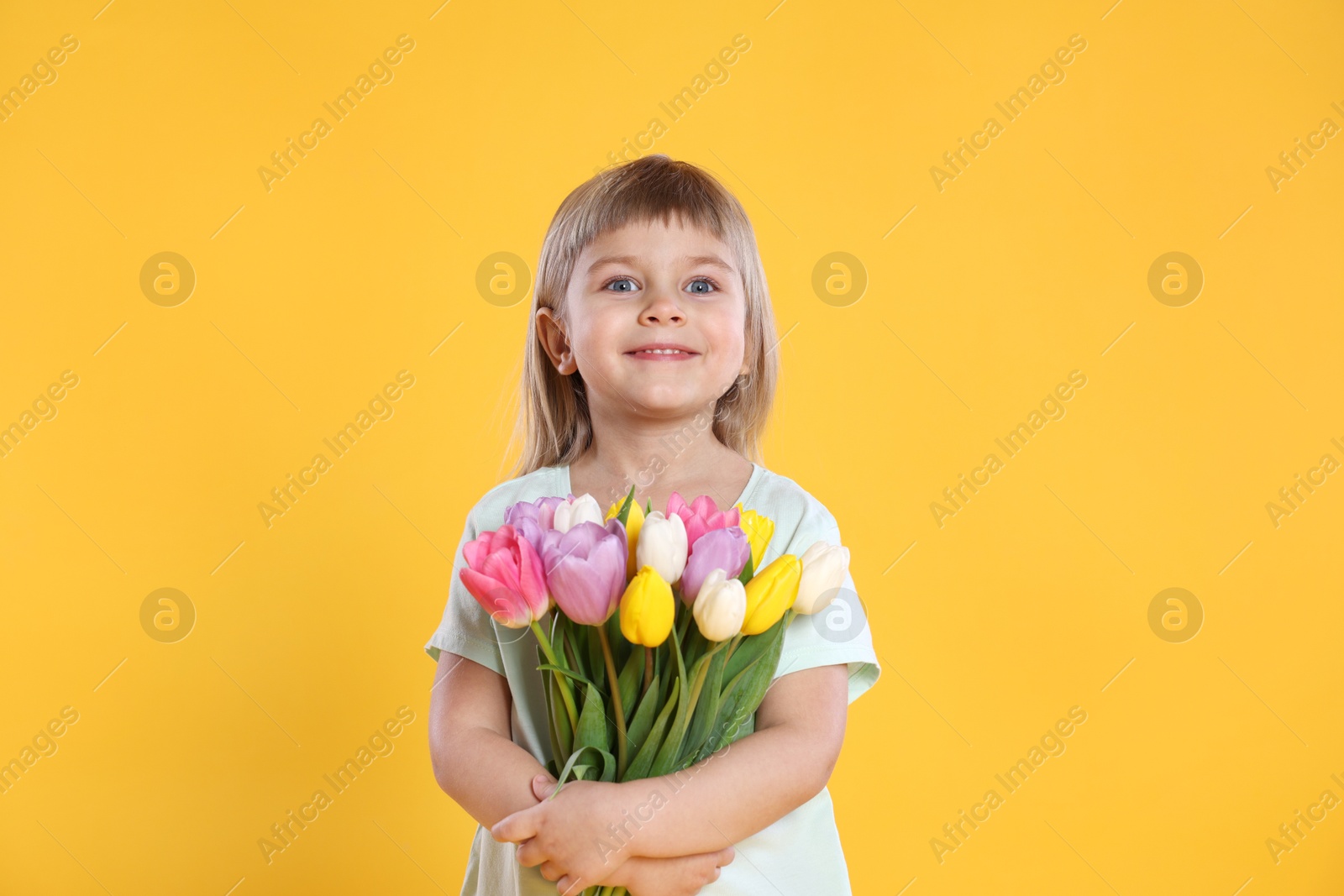 Photo of Smiling little girl with bouquet of tulips on yellow background