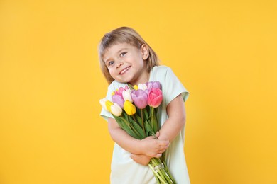 Photo of Smiling little girl with bouquet of tulips on yellow background