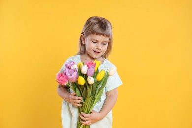 Photo of Cute little girl with bouquet of tulips on yellow background