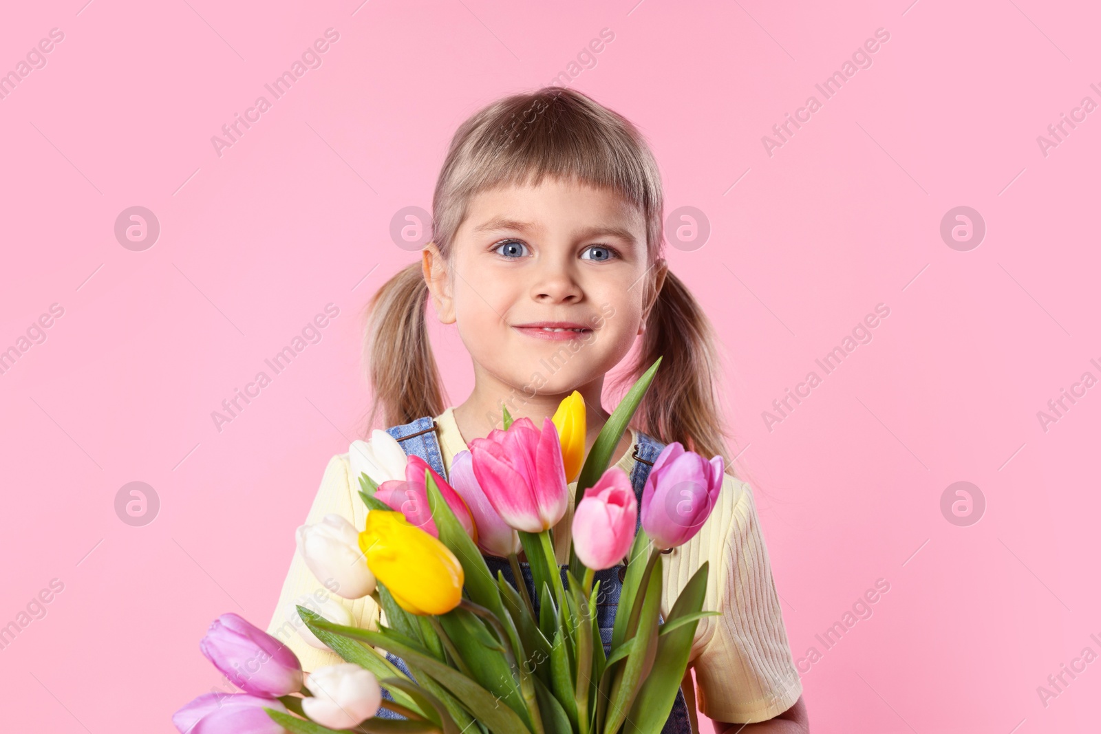 Photo of Cute little girl with bouquet of tulips on pink background