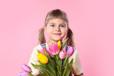 Photo of Cute little girl with bouquet of tulips on pink background