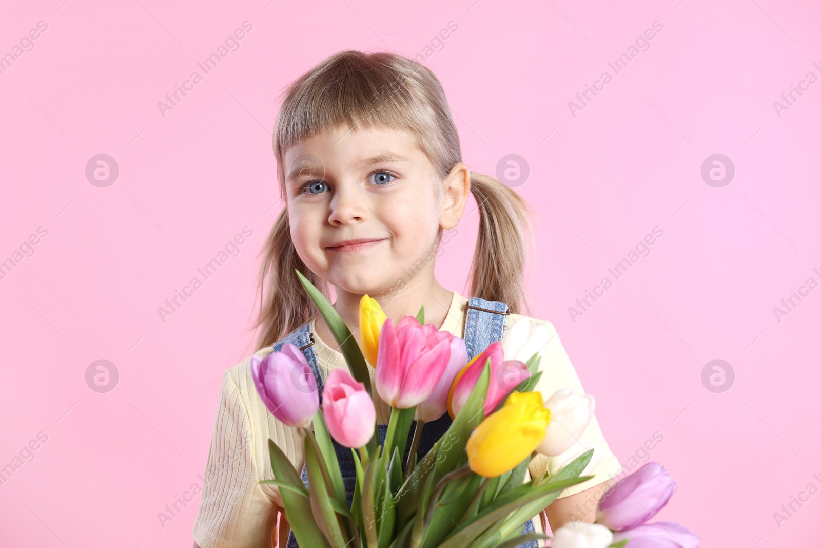 Photo of Cute little girl with bouquet of tulips on pink background