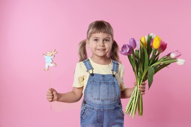 Photo of Smiling little girl with bouquet of tulips and decorative Easter bunny on pink background