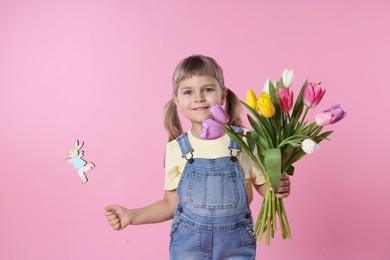 Photo of Happy little girl with bouquet of tulips and decorative Easter bunny on pink background