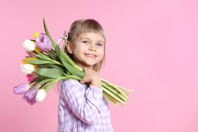 Photo of Smiling little girl with bouquet of tulips on pink background. Space for text