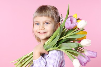 Photo of Smiling little girl with bouquet of tulips on pink background