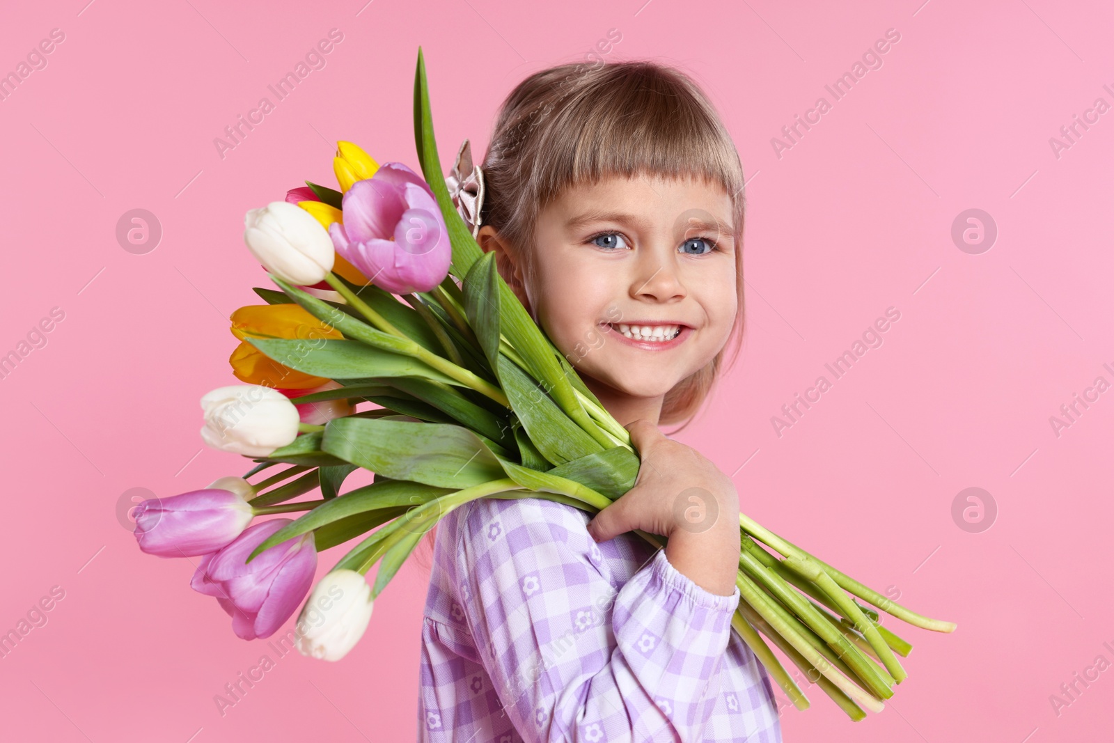 Photo of Smiling little girl with bouquet of tulips on pink background