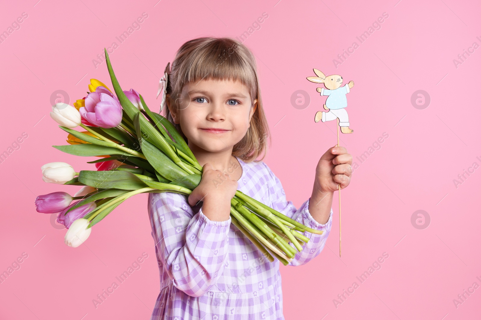 Photo of Cute little girl with bouquet of tulips and decorative Easter bunny on pink background