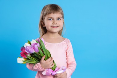 Photo of Smiling little girl with bouquet of tulips on light blue background. Space for text