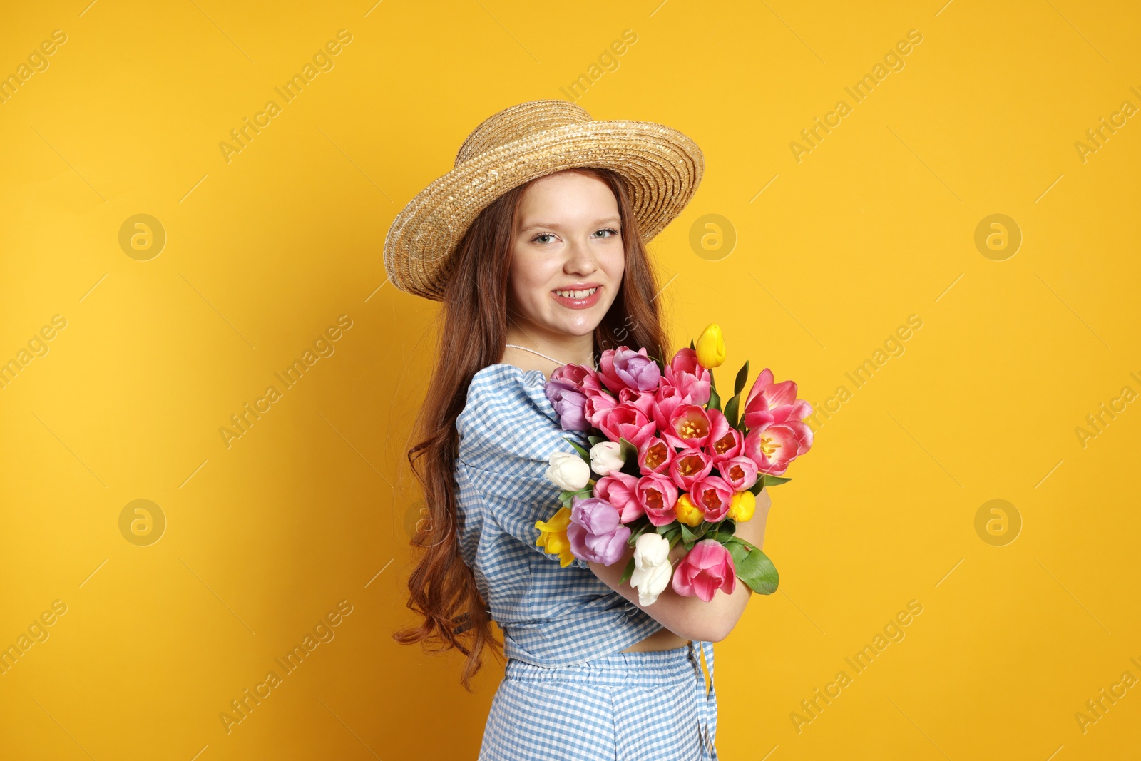 Photo of Beautiful teenage girl with bouquet of tulips on orange background