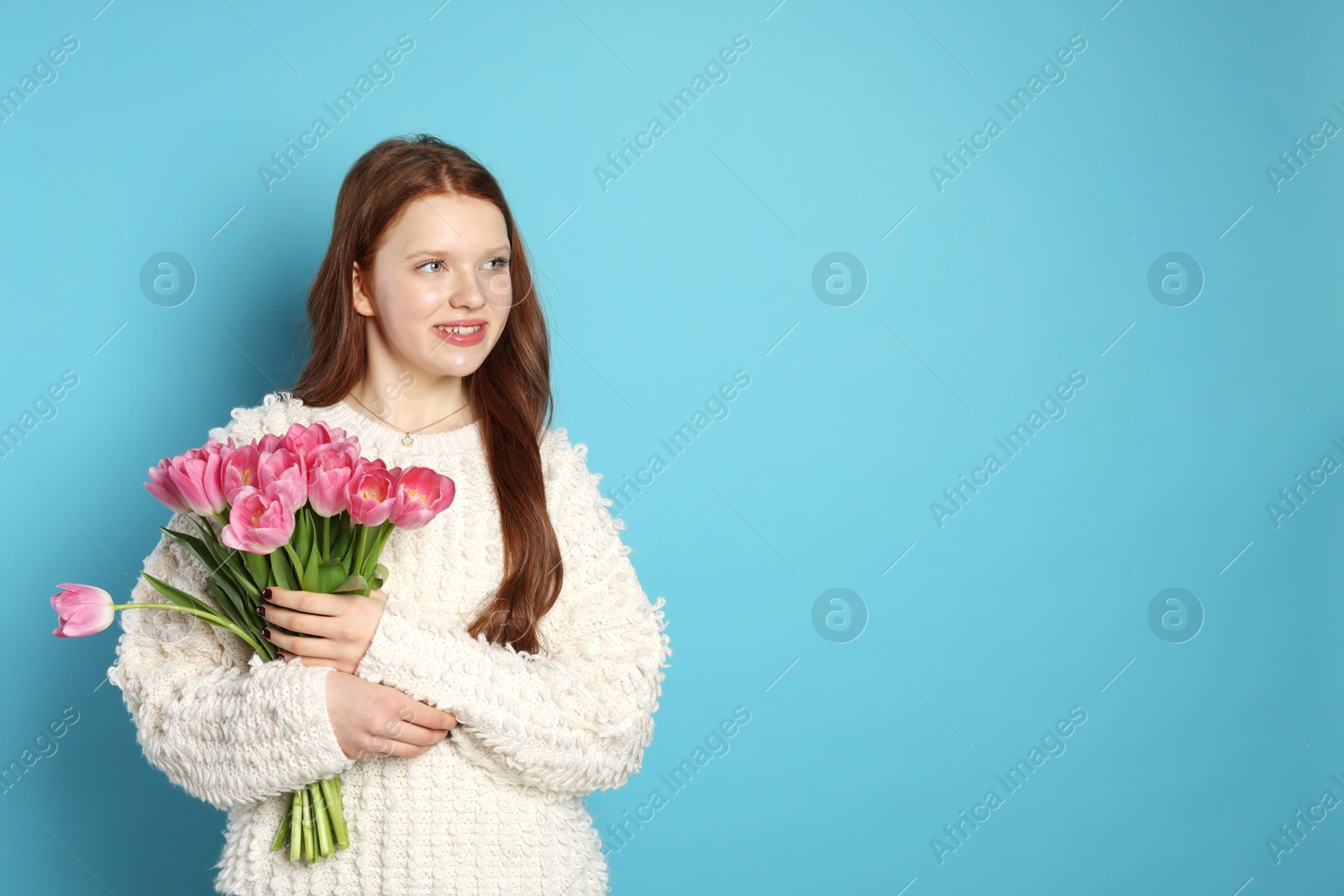 Photo of Beautiful teenage girl with bouquet of tulips on light blue background, space for text