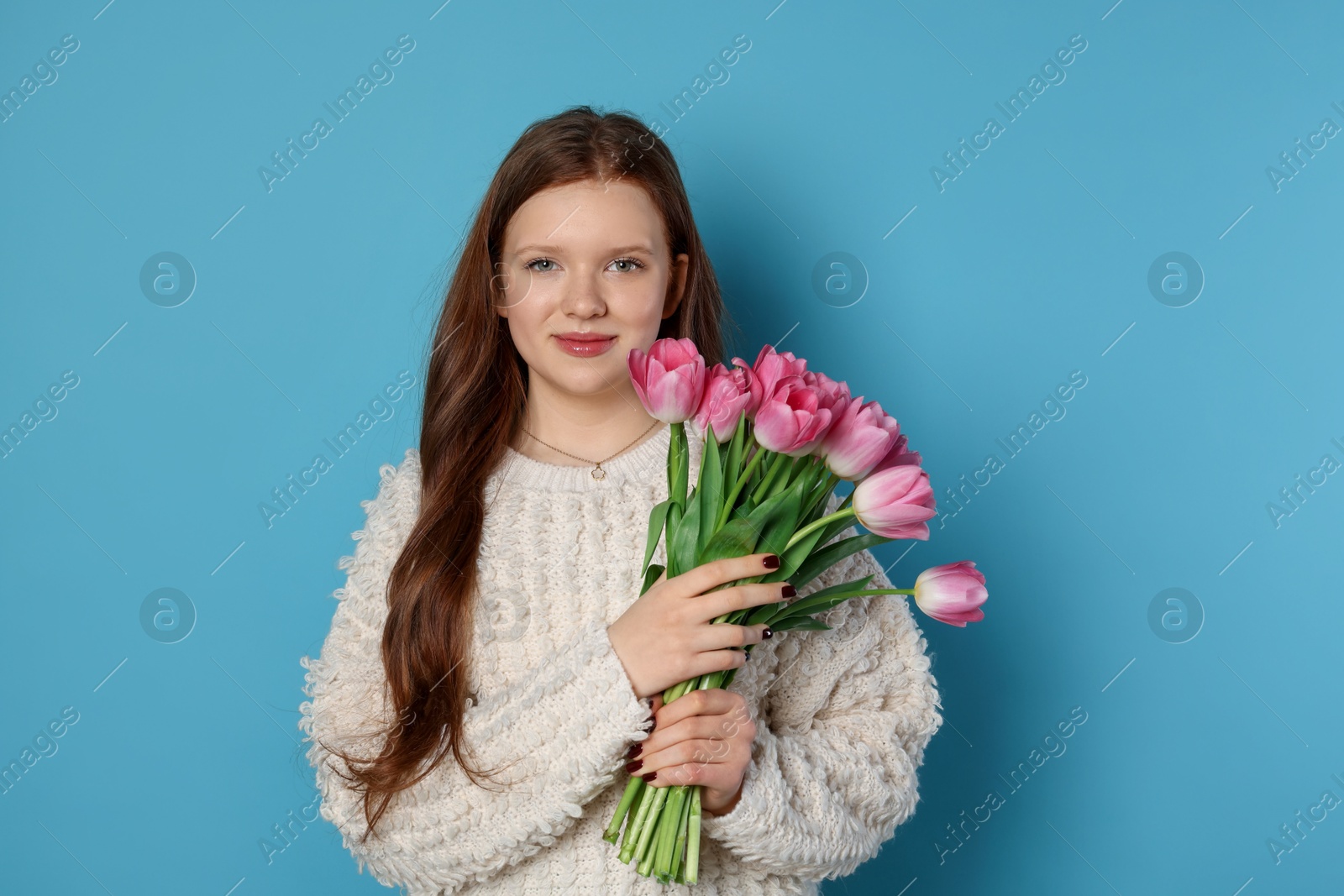 Photo of Beautiful teenage girl with bouquet of tulips on light blue background