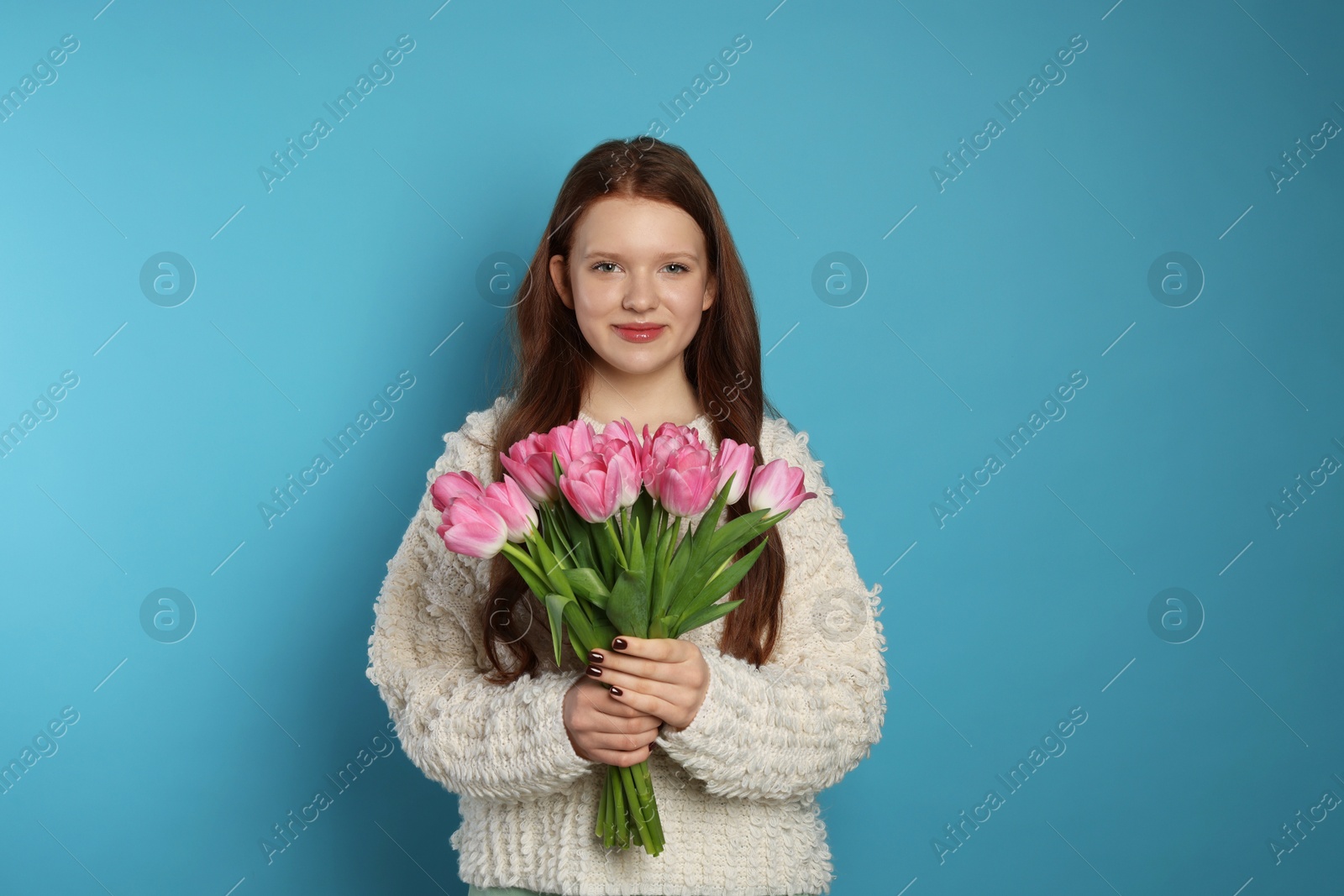 Photo of Beautiful teenage girl with bouquet of tulips on light blue background