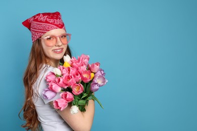 Photo of Beautiful teenage girl with bouquet of tulips on light blue background, space for text