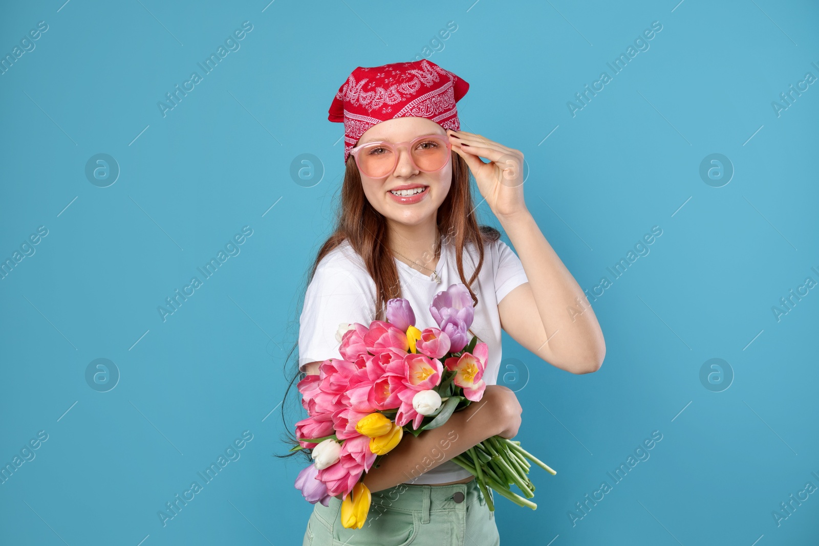 Photo of Beautiful teenage girl with bouquet of tulips on light blue background