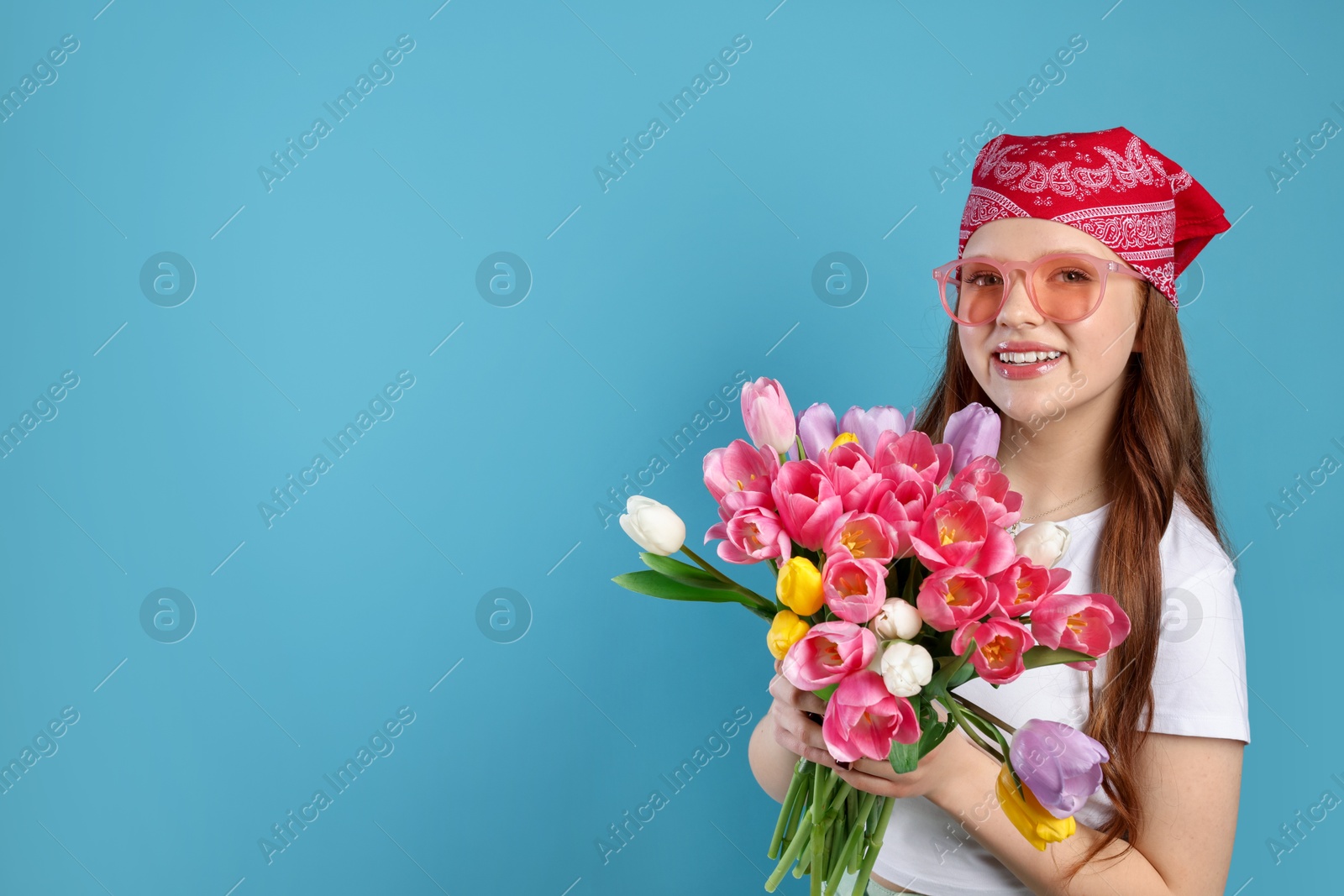 Photo of Beautiful teenage girl with bouquet of tulips on light blue background, space for text