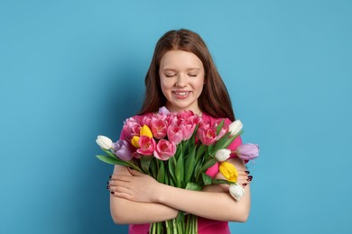 Photo of Beautiful teenage girl with bouquet of tulips on light blue background