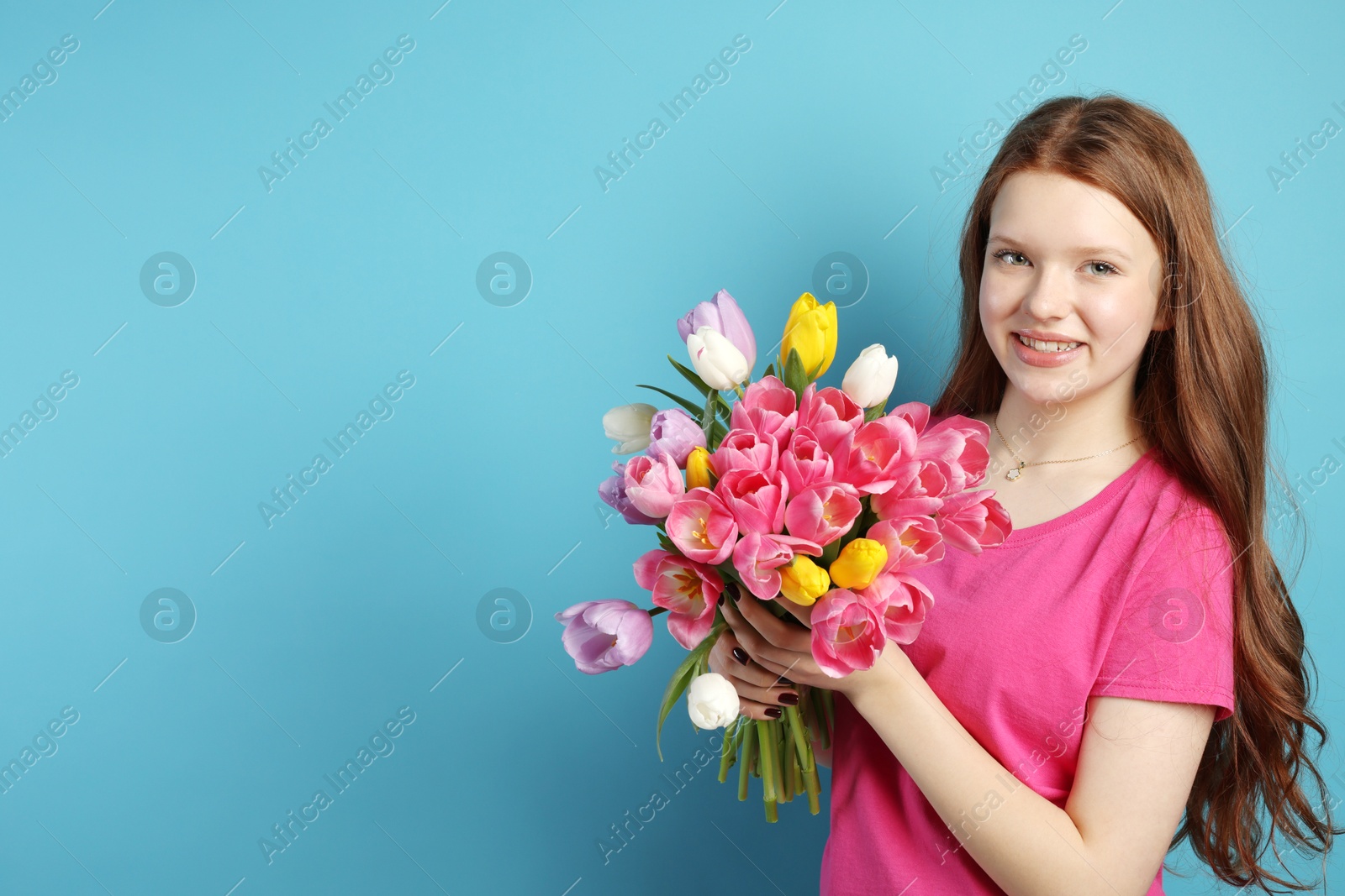 Photo of Beautiful teenage girl with bouquet of tulips on light blue background, space for text