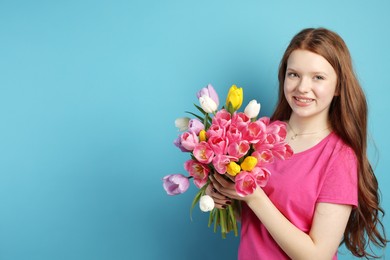 Photo of Beautiful teenage girl with bouquet of tulips on light blue background, space for text