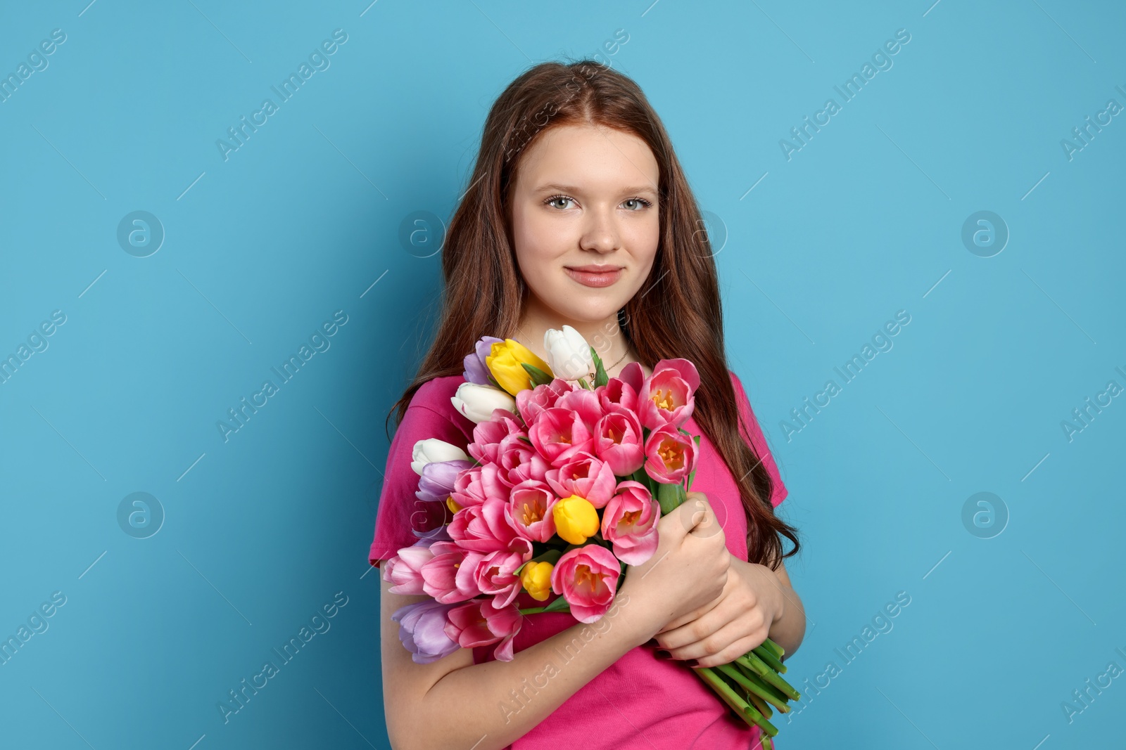 Photo of Beautiful teenage girl with bouquet of tulips on light blue background