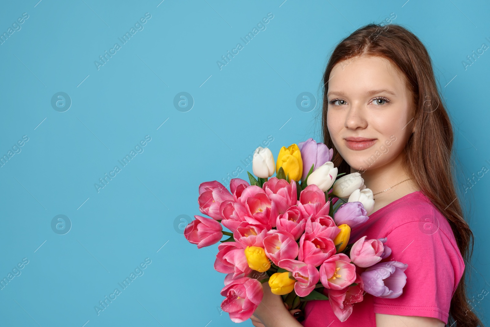 Photo of Beautiful teenage girl with bouquet of tulips on light blue background, space for text