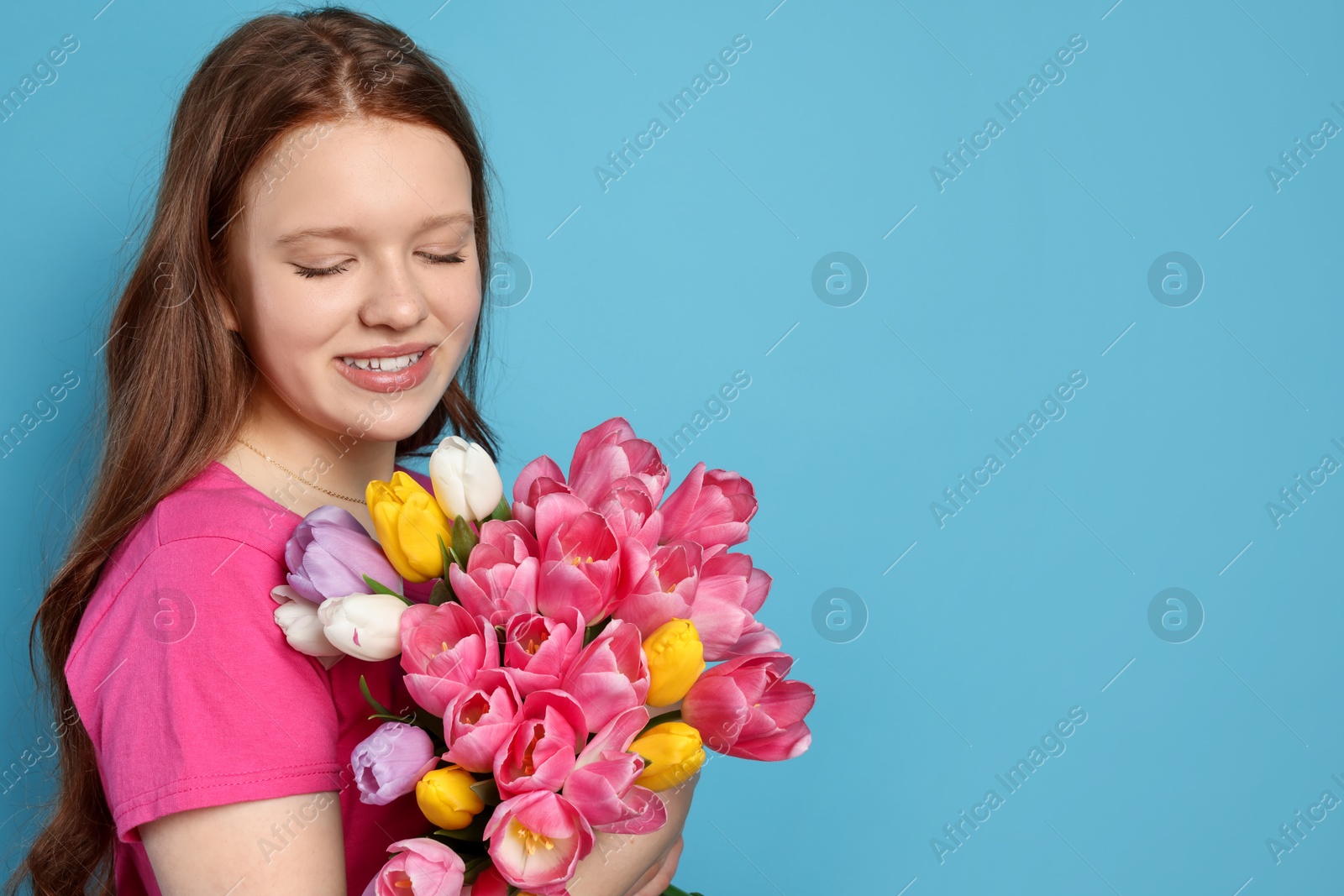 Photo of Beautiful teenage girl with bouquet of tulips on light blue background, space for text