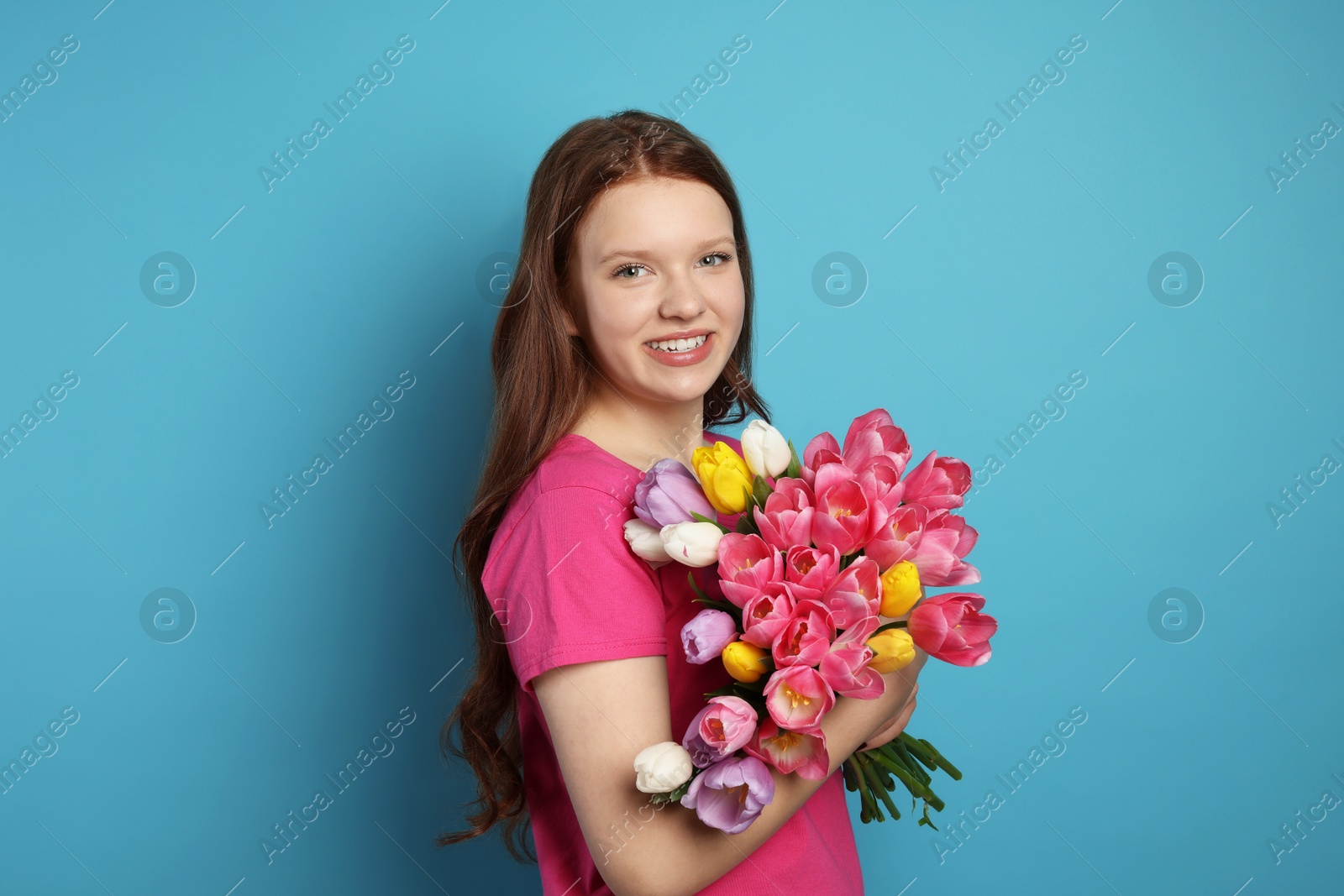 Photo of Beautiful teenage girl with bouquet of tulips on light blue background