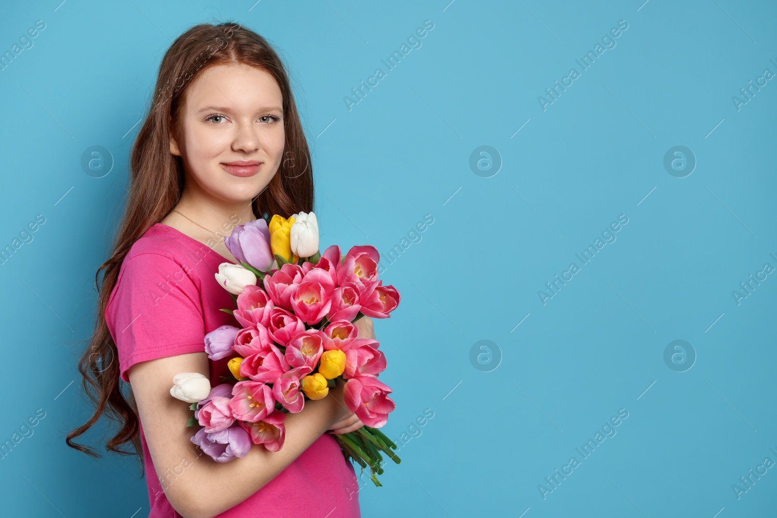 Photo of Beautiful teenage girl with bouquet of tulips on light blue background, space for text