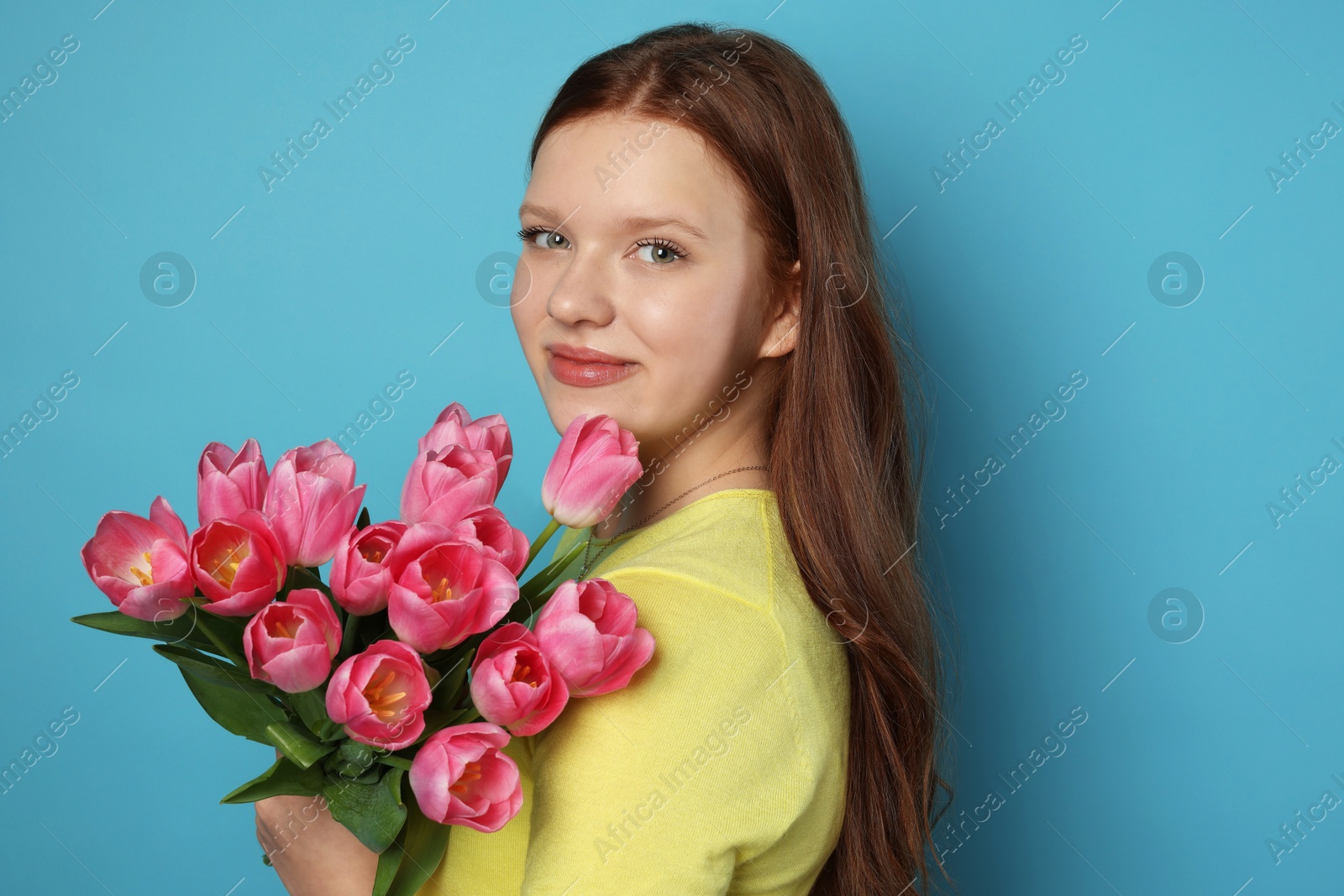 Photo of Beautiful teenage girl with bouquet of tulips on light blue background