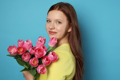 Photo of Beautiful teenage girl with bouquet of tulips on light blue background