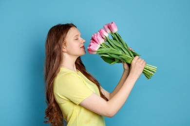 Photo of Beautiful teenage girl with bouquet of tulips on light blue background