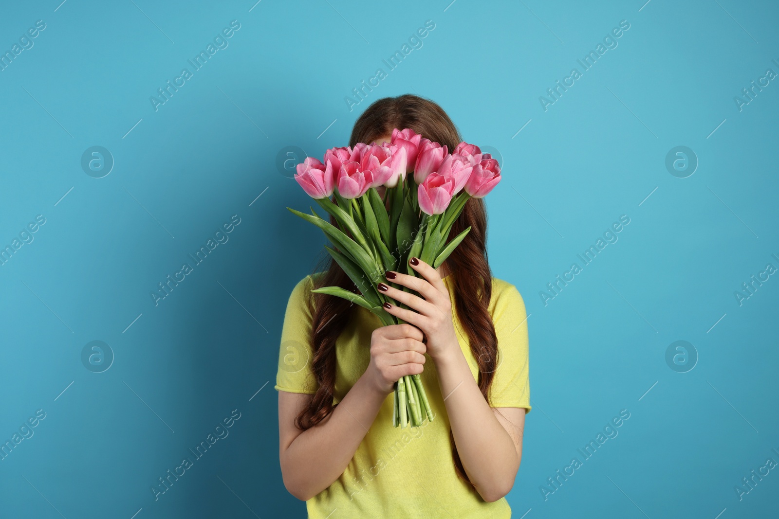 Photo of Teenage girl with bouquet of tulips on light blue background