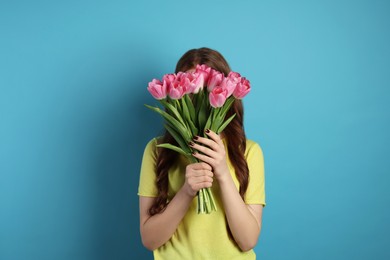 Photo of Teenage girl with bouquet of tulips on light blue background