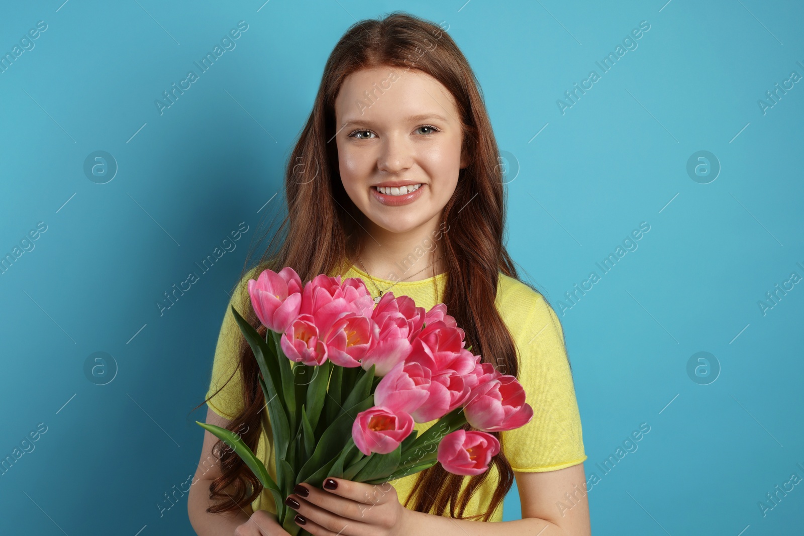 Photo of Beautiful teenage girl with bouquet of tulips on light blue background