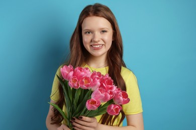 Photo of Beautiful teenage girl with bouquet of tulips on light blue background