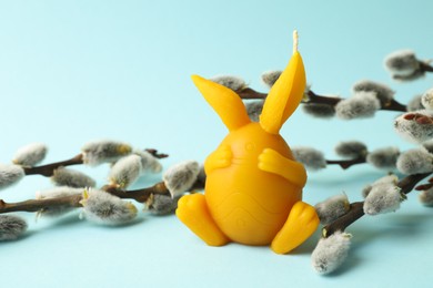 Photo of Beautiful candle and pussy willow on light blue background, closeup. Easter decor